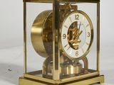 a gold clock in a glass case on a white surface