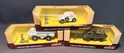 trois jouets représentant des véhicules militaires, dans leurs boîtes, posés sur une surface grise