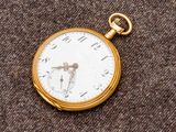 une montre de poche en or avec un cadran blanc sur un fond marron