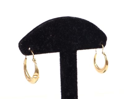 une paire de boucles d'oreilles créoles en or posées sur un support en velours noir, sur fond blanc