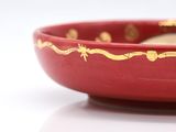 a red bowl with gold designs on it on a white surface