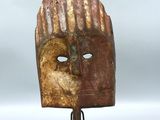 un masque en bois posé sur un socle en métal, sur une surface blanche