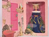 une poupée dans une boîte rose sur laquelle figure l'image d'une femme vêtue d'une robe bleue et portant des bijoux en or