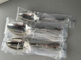 four silver spoons are wrapped in clear plastic bags on a table
