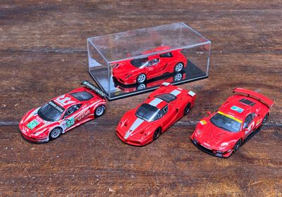 quatre petites voitures rouges dans une vitrine posée sur une table en bois