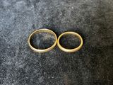 two gold wedding rings sitting on top of a black surface