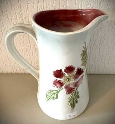 un pichet blanc orné de fleurs rouges, posé sur une table
