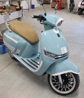 un scooter bleu garé dans un garage, avec d'autres scooters en arrière-plan