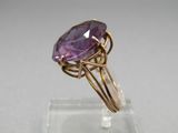a close up of a ring with a purple stone on a clear surface