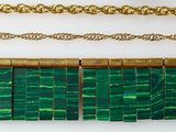 a close up of a row of green and gold necklaces on a white surface