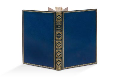 un livre bleu ouvert, aux bords dorés, posé sur une surface blanche
