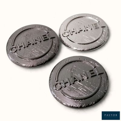 trois boutons en métal noir et argent portant l'inscription « Chanel »