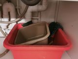 a red container with a brush in it under a sink