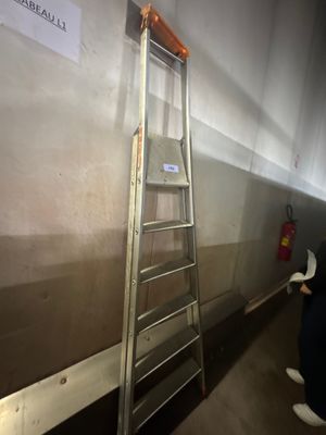une échelle appuyée contre un mur, sur laquelle est accrochée une pancarte