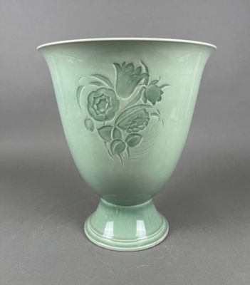 a green vase with flowers on it on a gray surface