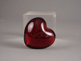 un objet en verre rouge en forme de cœur, placé dans une boîte transparente