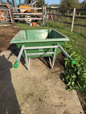 une brouette verte au milieu d'un champ de terre battue