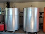 trois grandes cuves métalliques dans un garage, à côté de fûts orange