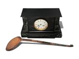 a small black clock with a wooden spoon next to it