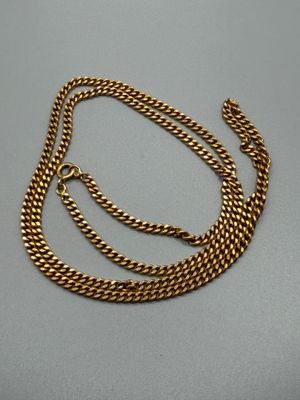 un collier à chaîne en or posé sur une surface grise