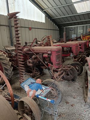 many old tractors in a barn with a man standing next to them