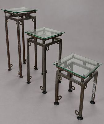 trois tables avec un plateau en verre et des pieds en métal, sur fond gris
