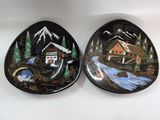 two decorative plates with a cabin and a stream in the background