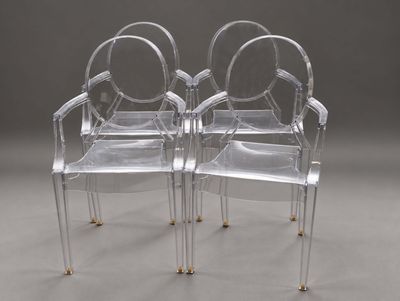 deux chaises en plastique transparent avec des pieds et des accoudoirs dorés, posées sur une surface grise