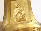 a gold clock on a wooden table with a white wall in the background