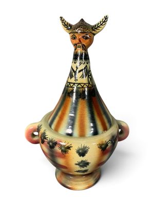 un vase surmonté d'un oiseau, posé sur une surface blanche