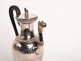 a silver vase with a black handle on a table