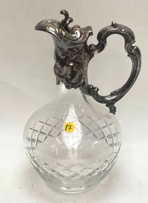 un vase en verre muni d'une poignée en argent, posé sur une table