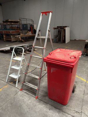 a red trash can next to a ladder in a warehouse