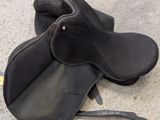 a black saddle and a pair of black boots on the ground