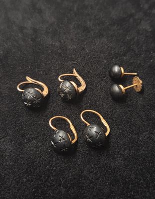 un lot de cinq boucles d'oreilles en pierre dorée et noire, posées sur un fond noir