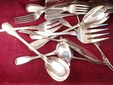 a lot of silver spoons and forks on a red cloth