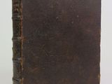 an old brown book sitting on top of a table next to a white wall