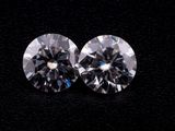 a pair of round cut diamonds on a black surface