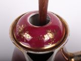 a red and gold vase with a wooden handle
