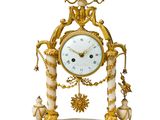 une horloge dorée et blanche posée sur un socle, sur une surface blanche