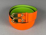 une ceinture orange et verte ornée de deux boucles dorées sur un fond gris