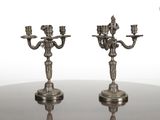 une paire de bougeoirs anciens en métal argenté posés sur une table en verre