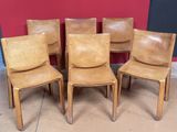 Quatre fauteuils en cuir sont alignés contre un mur rouge