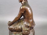bronze statue of a woman sitting on a rock with her legs crossed