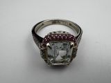 a close up of a diamond and ruby ring on a white surface