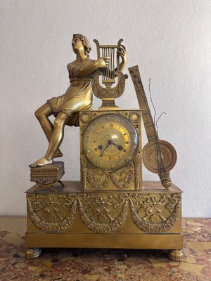 a gold clock with a woman playing a musical instrument on it