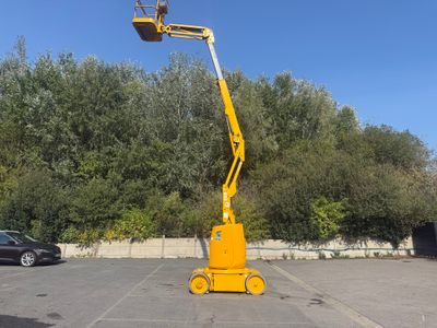 La grue jaune est garée sur le parking, près des arbres.