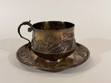 une tasse et une soucoupe anciennes en argent, posées sur une soucoupe