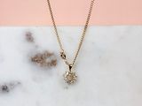 un collier en or orné d'un pendentif en forme de fleur sertie d'un diamant, posé sur une surface en marbre
