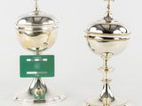 two silver cups with crosses on top of them and a green tag
